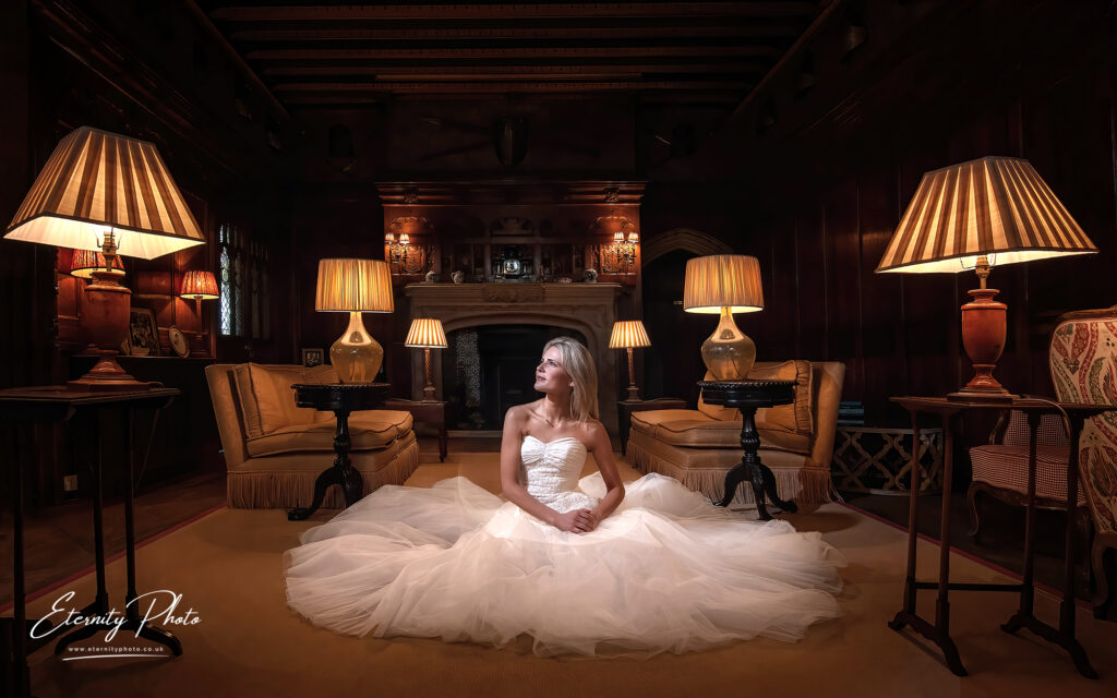 A woman in a white bridal gown sitting on the floor of an elegant room lit by table lamps.