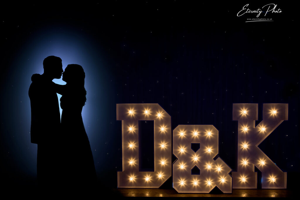 Silhouetted couple posing with illuminated initials under a spotlight against a starry background.