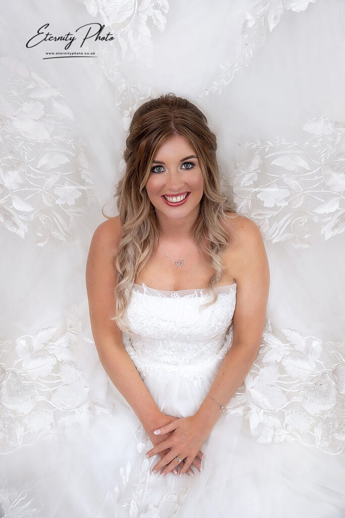 Bride smiling for a portrait, surrounded by her white, lacy wedding dress.