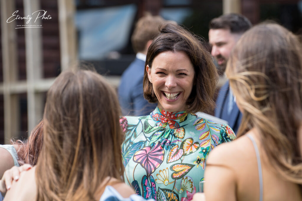 A woman in a floral dress smiling and conversing with others at a social event.