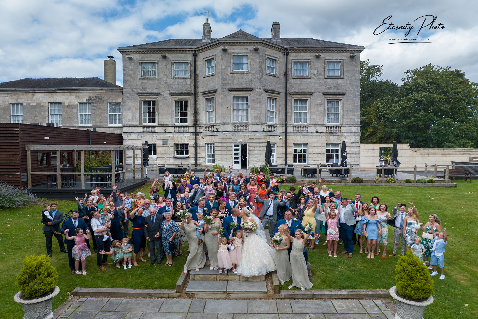 Wedding guests celebrating outside historic manor in UK.