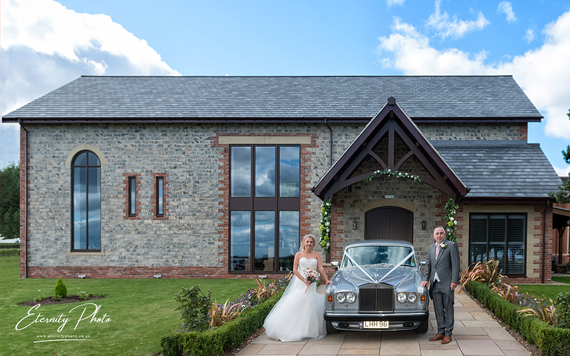 Bride, groom, vintage car outside stone building.