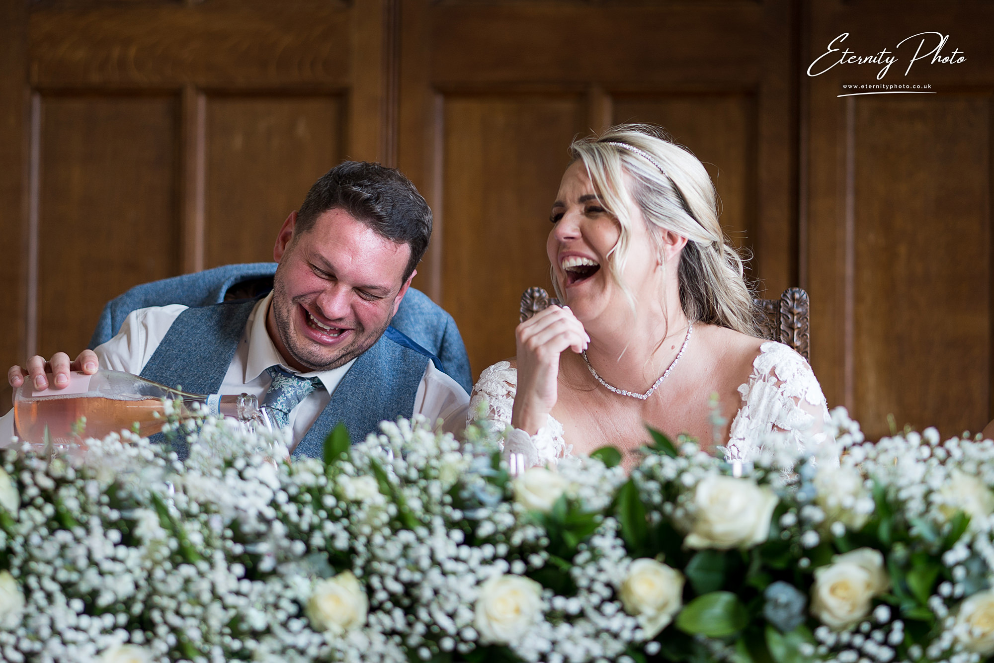Joyful wedding couple laughing at reception table.