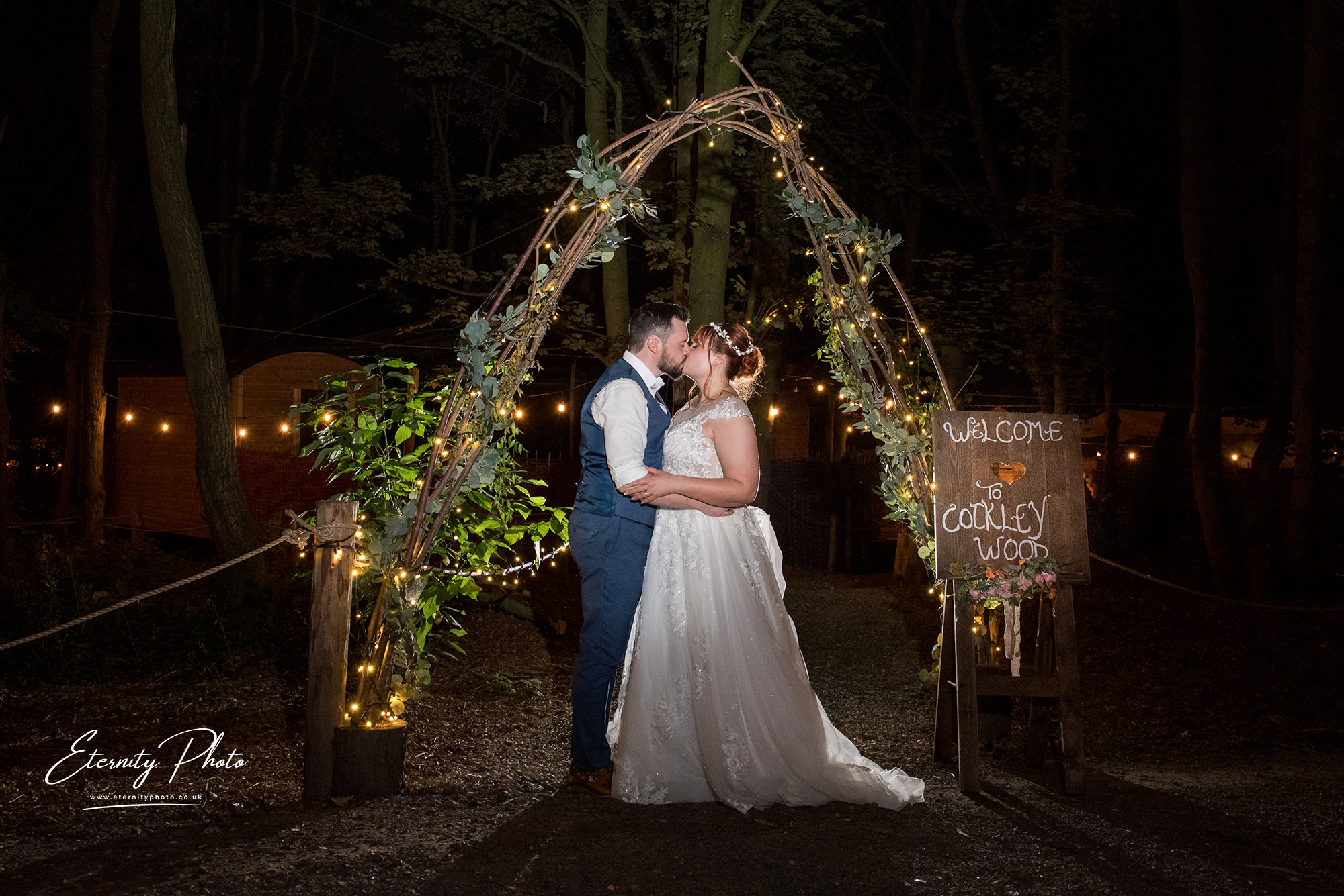 Couple kissing under lighted archway at night wedding.