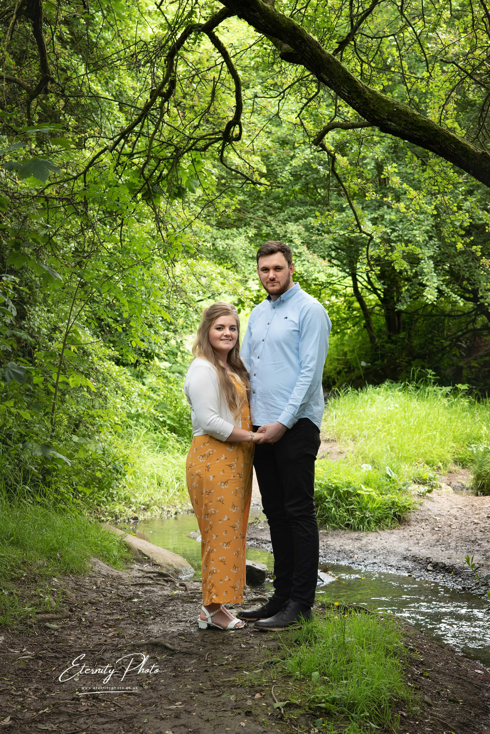 Couple posing in serene woodland by stream.