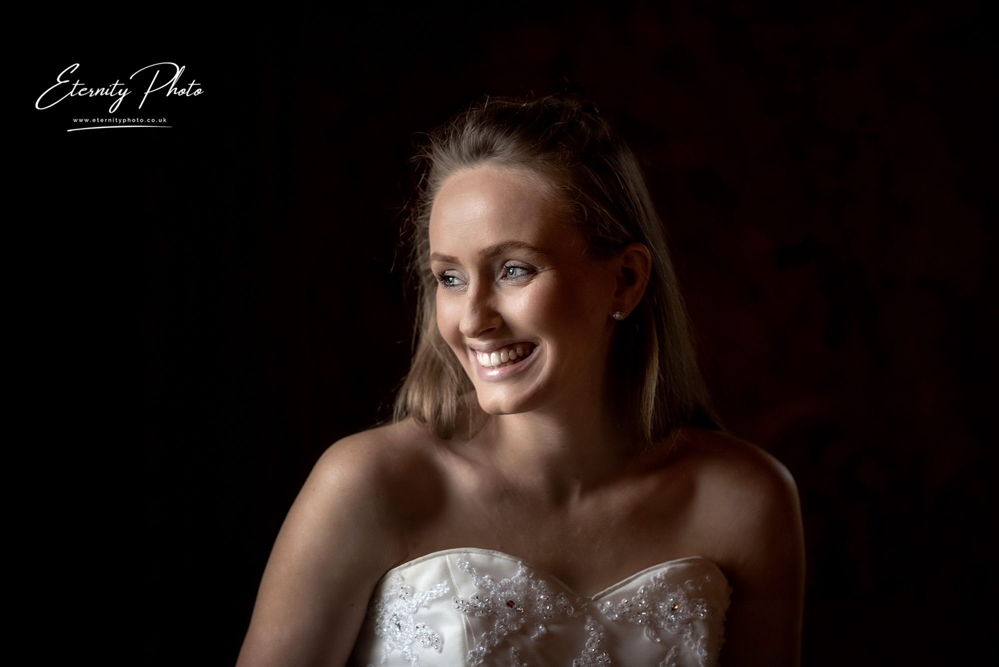Bride smiling gently in dimly lit room.