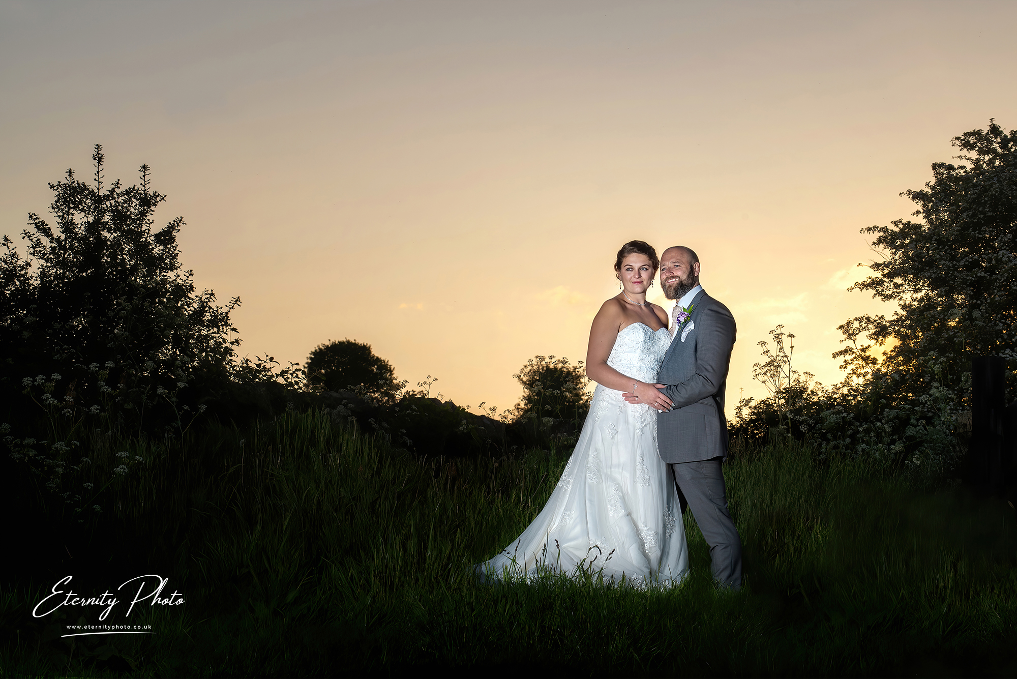 Couple in wedding attire during sunset in a field.