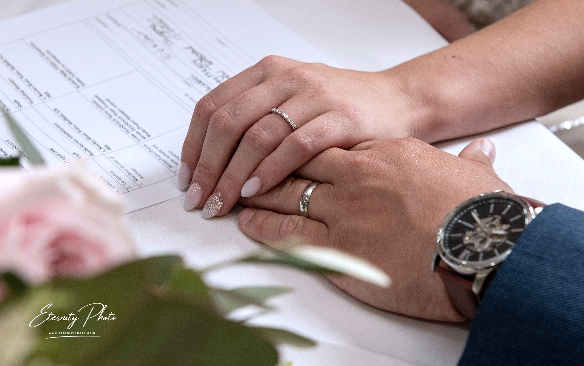 Couple's hands with wedding rings, signing registry.