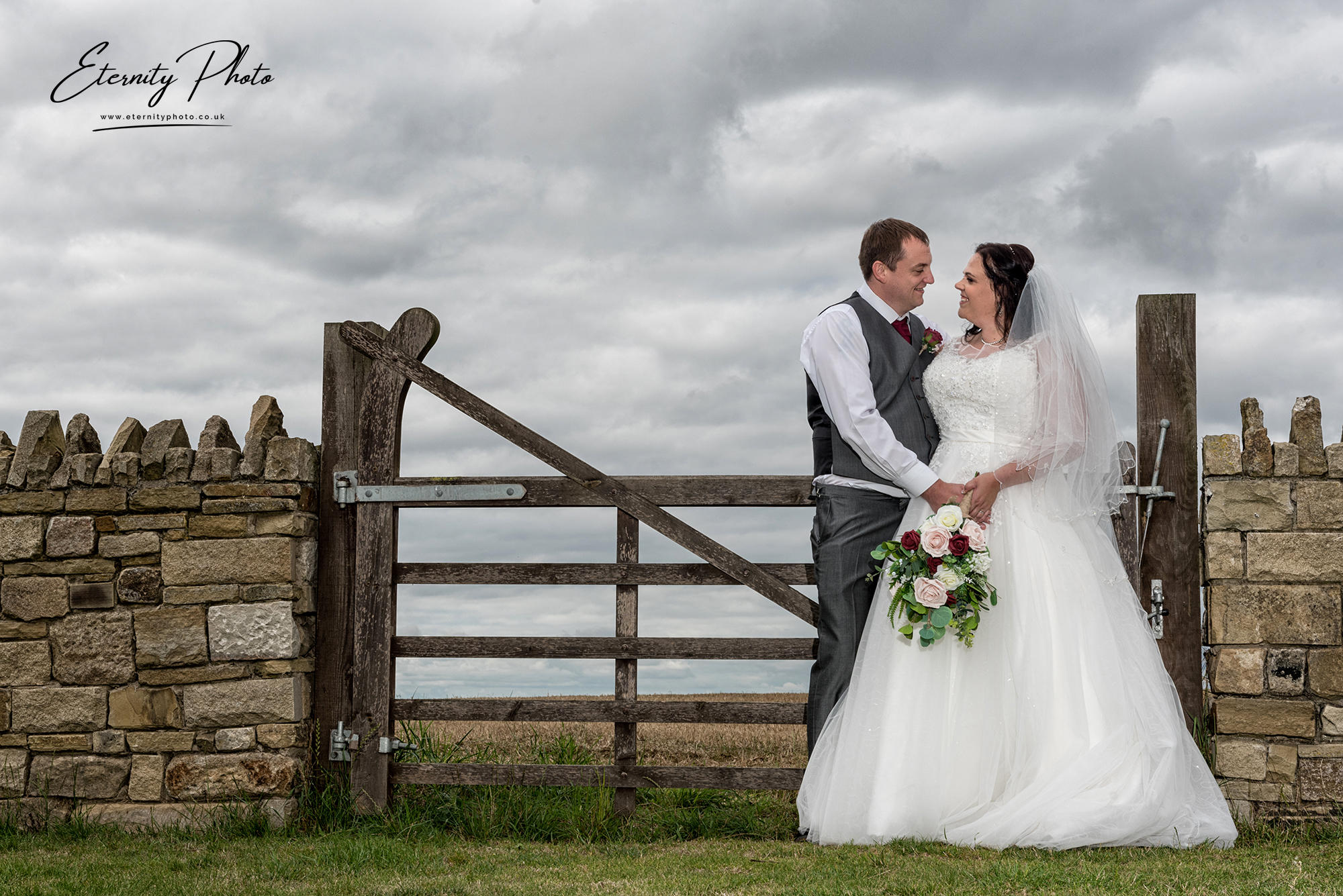 Bride and groom embracing by countryside gate.