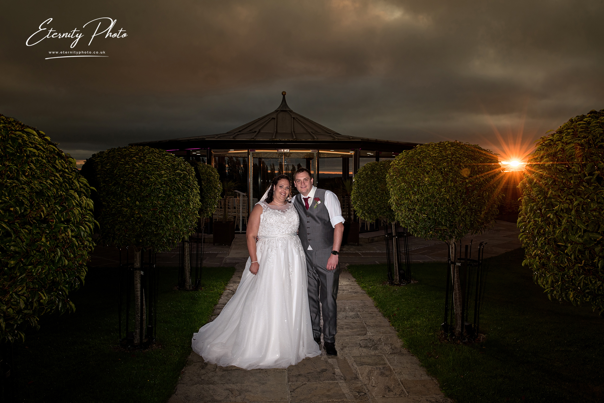 Bride and groom posing at sunset outside wedding venue.