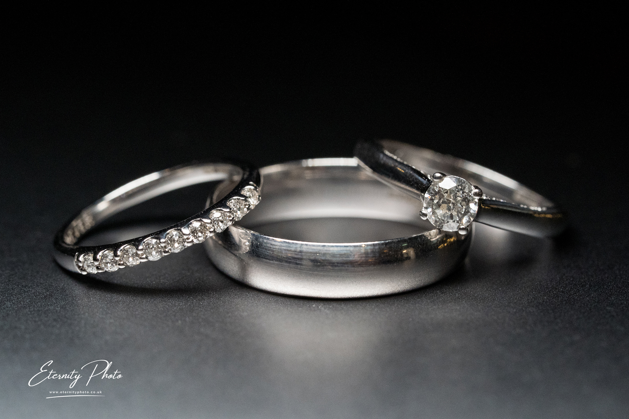 Diamond engagement and wedding rings on dark background.