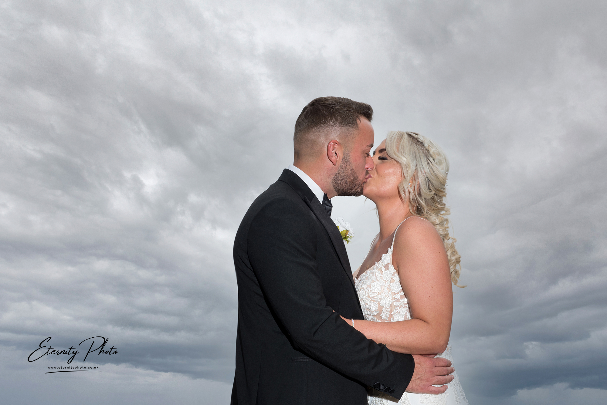 Bride and groom kissing under stormy skies.