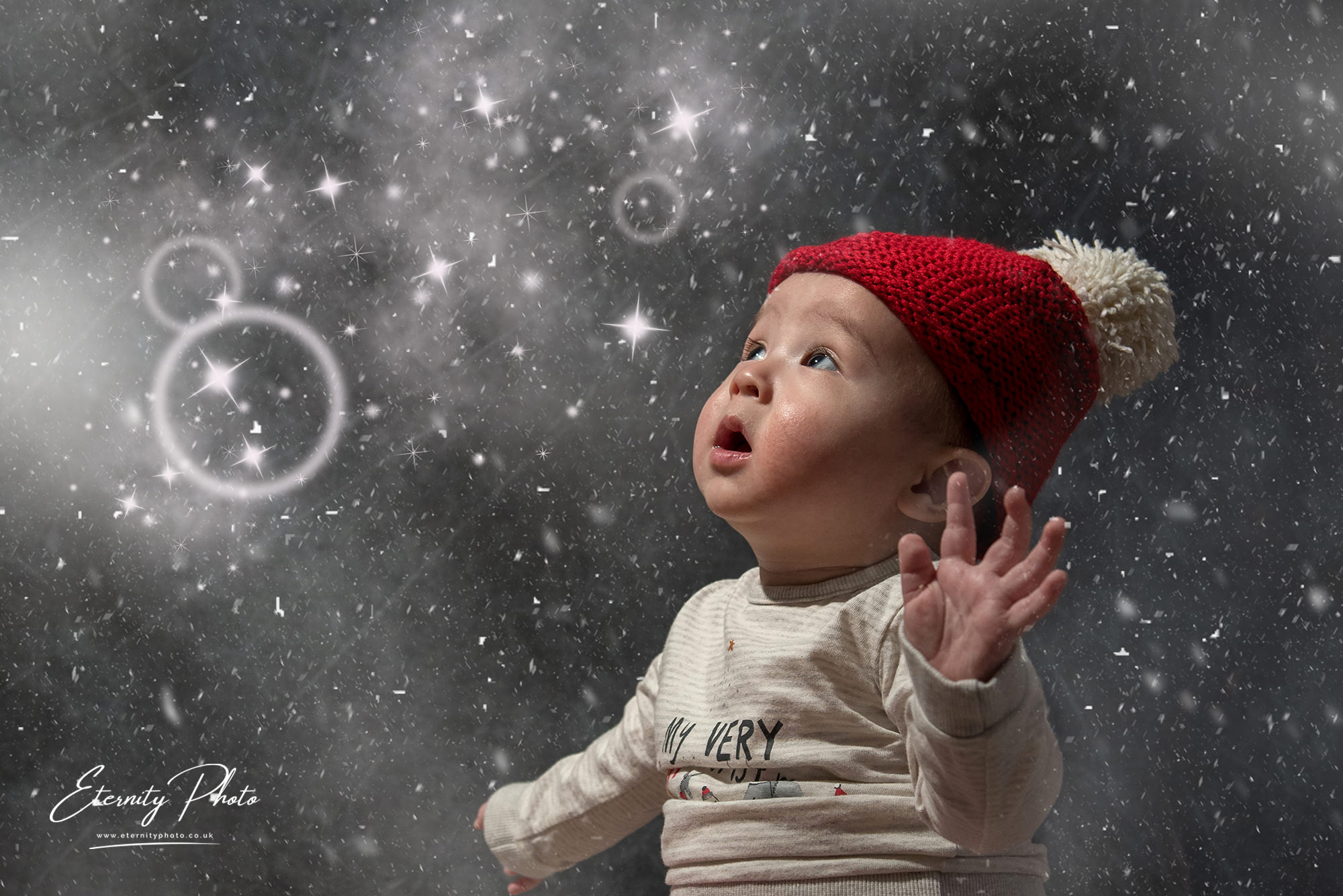 Baby in red hat amazed by snowflakes and stars