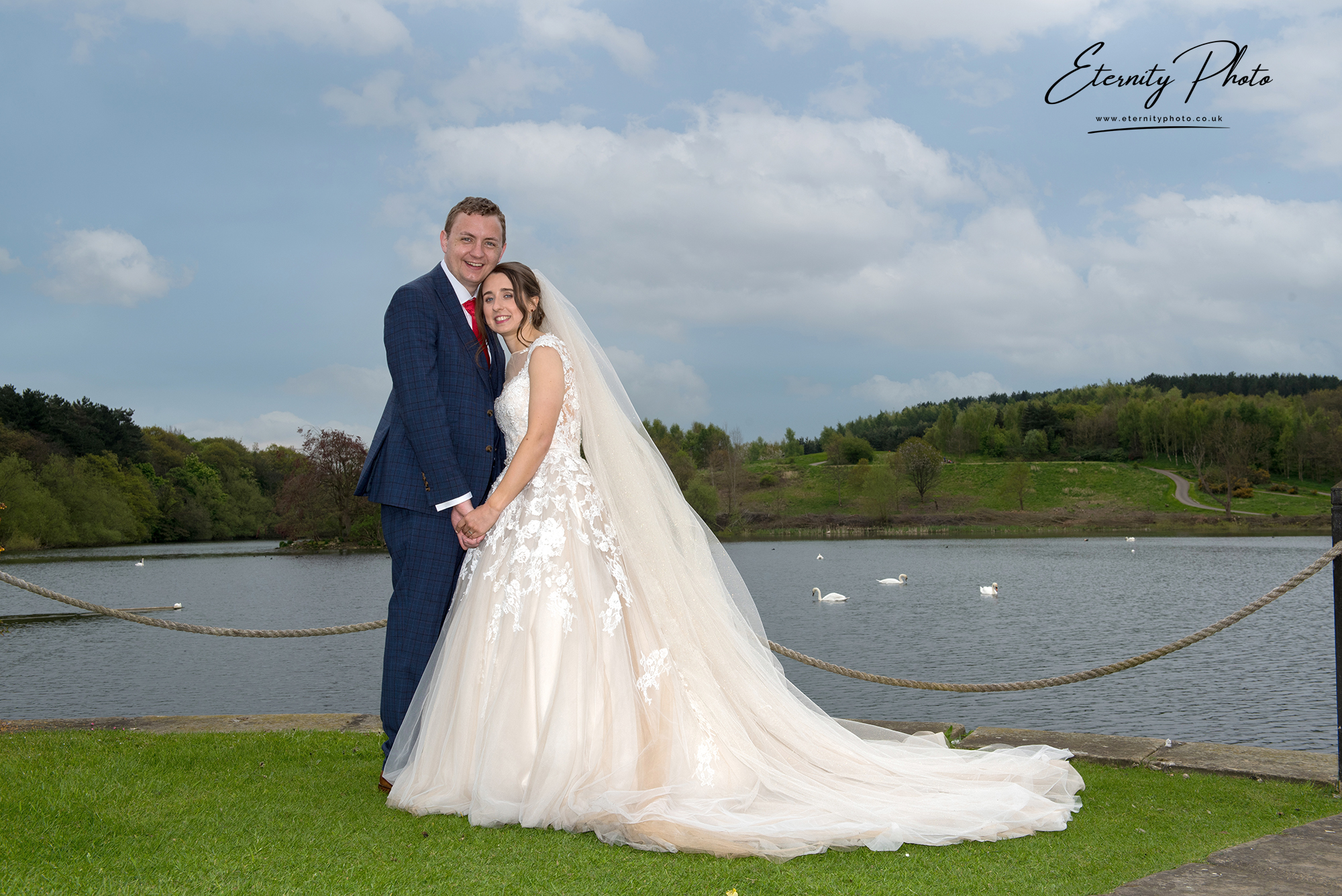 Couple at lakeside wedding with swans in background.