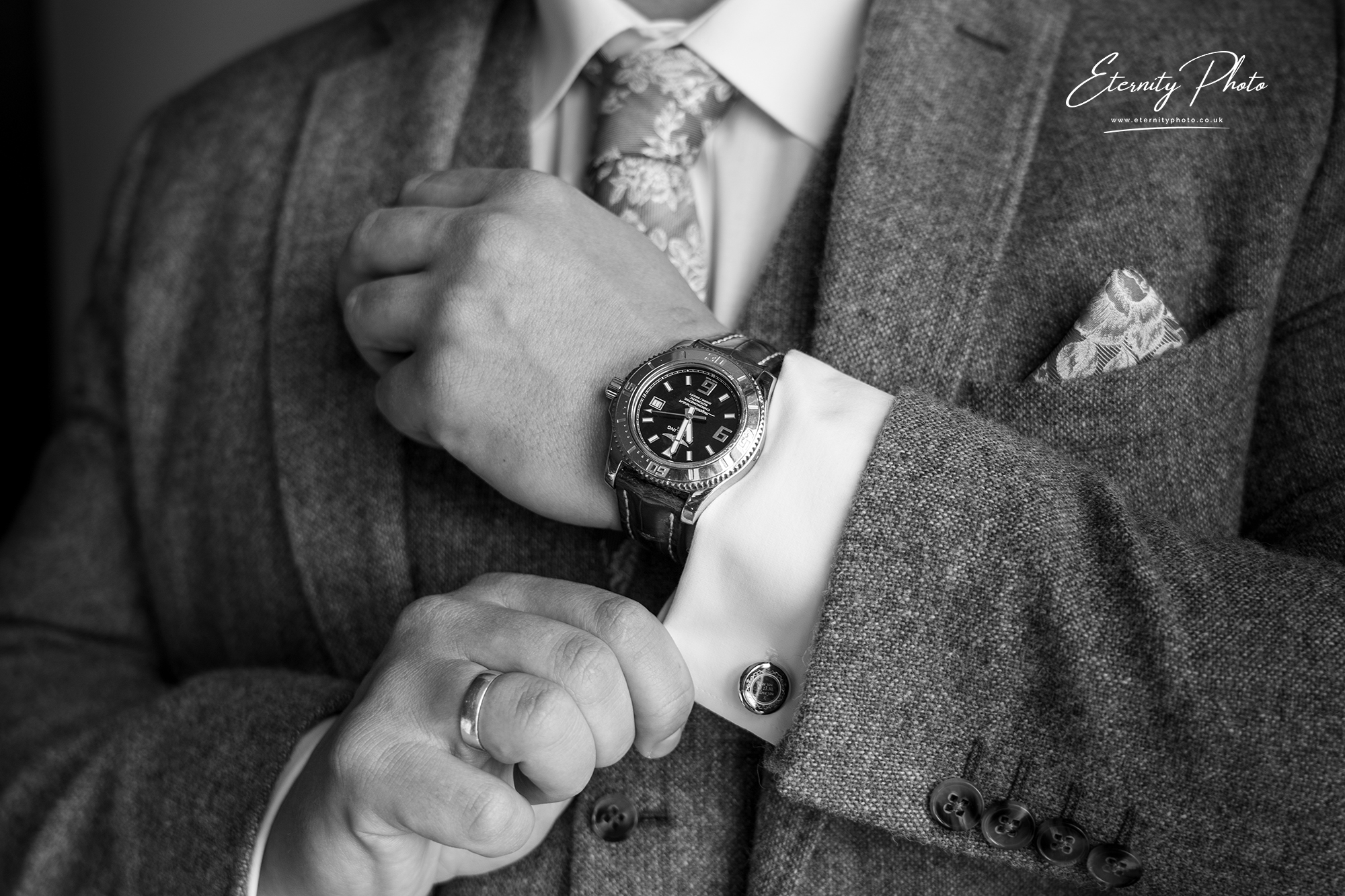 Man adjusting cufflink, wearing watch and suit.