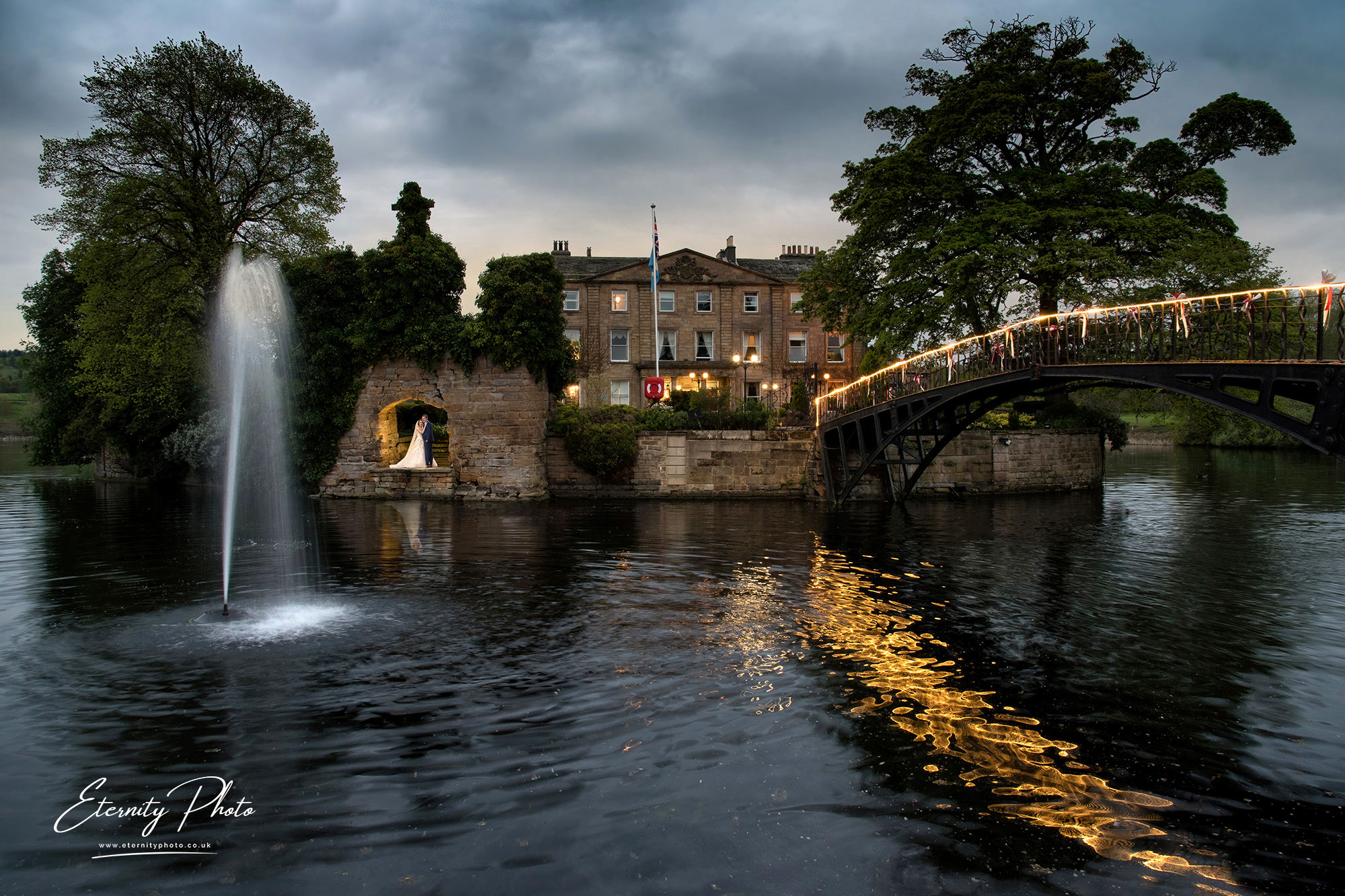 Evening river scene with illuminated bridge and fountain.