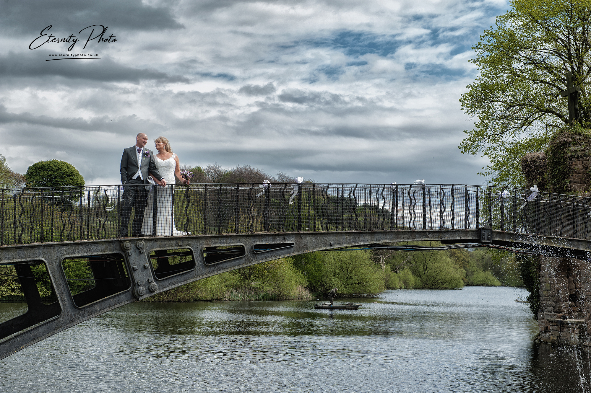 Bridal couple posing on picturesque metal bridge over river.