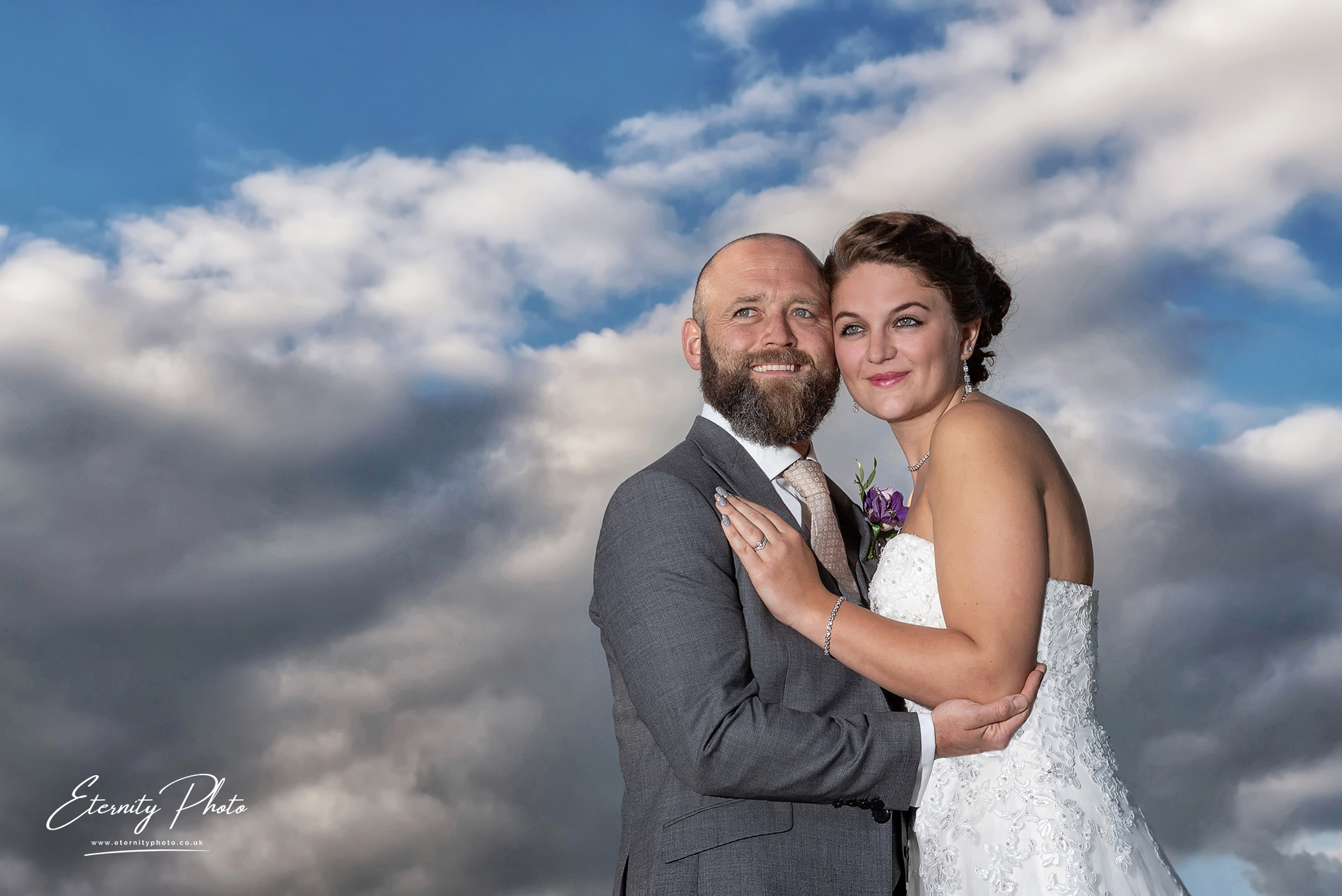 Bride and groom embrace under cloudy sky