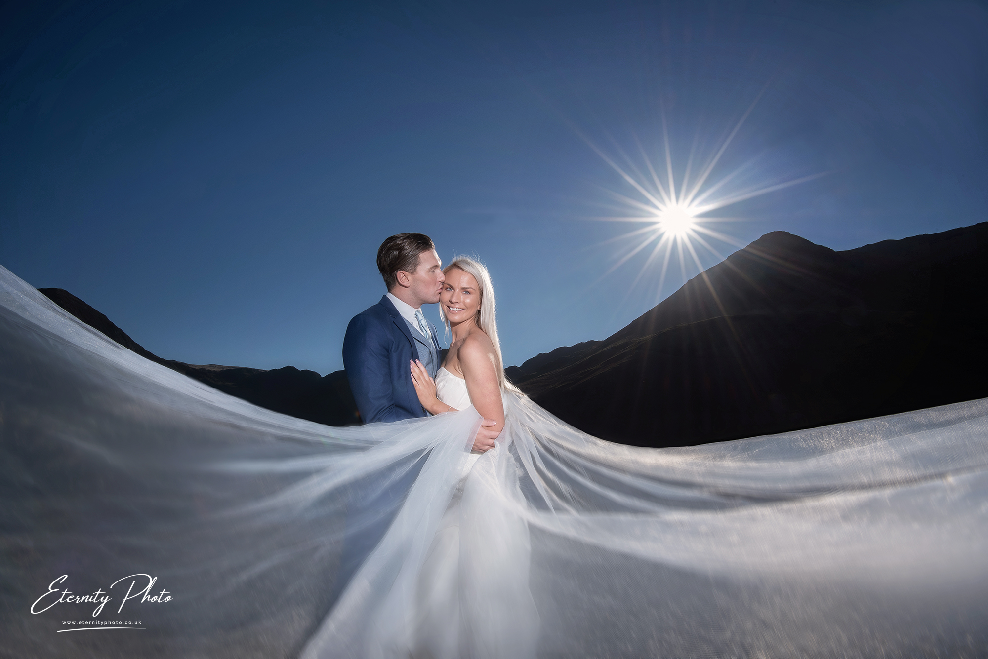 Bride and groom embracing in mountains with flowing veil