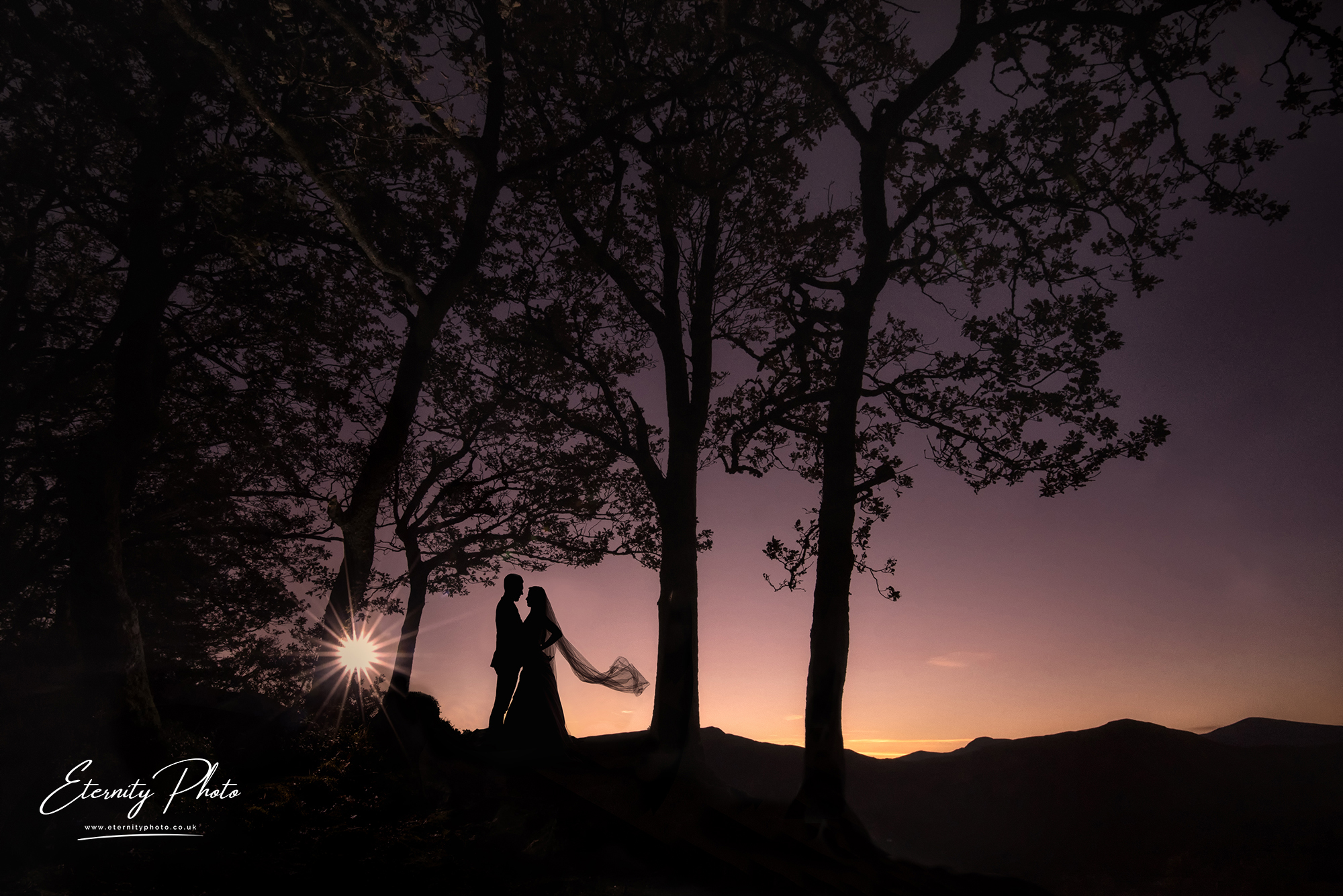 Couple silhouette at sunset with trees and hills.